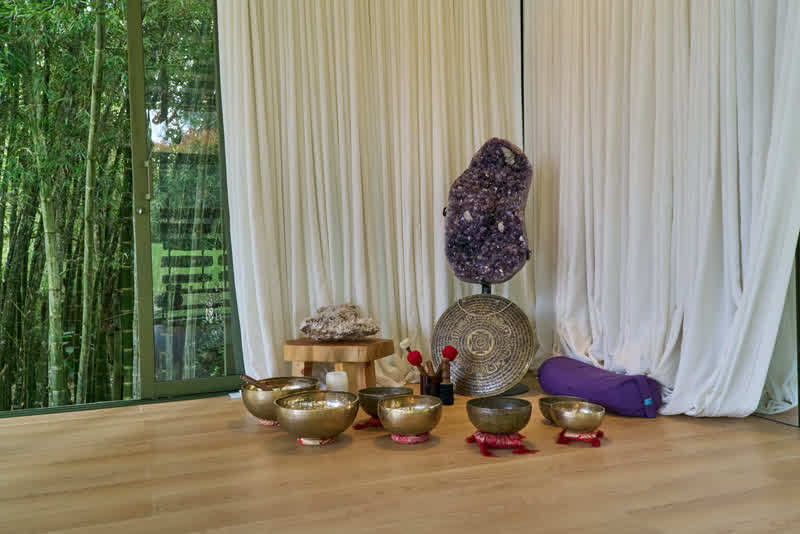 Cuencos tibetanos y geoda de amatista frente al ventanal con bambú, para sesiones de meditación con soundhealing