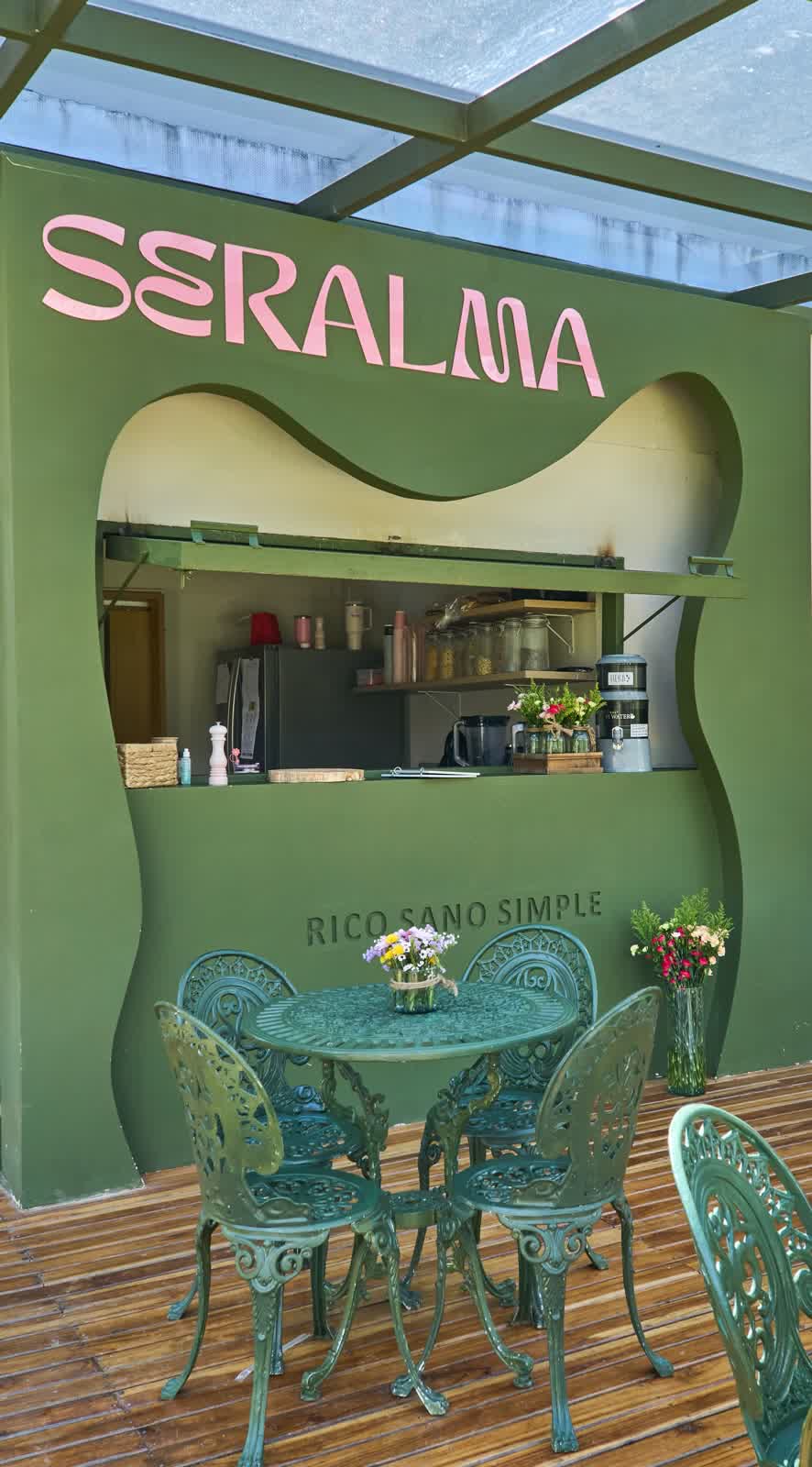 Fachada del café Seralma en EYOWA: barra verde con el letrero Seralma y mesas de hierro forjado en el deck de madera